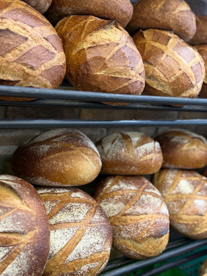 services-02 Delicious artisan bread loaves stacked on shelves in a bakery, showcasing crusty textures.